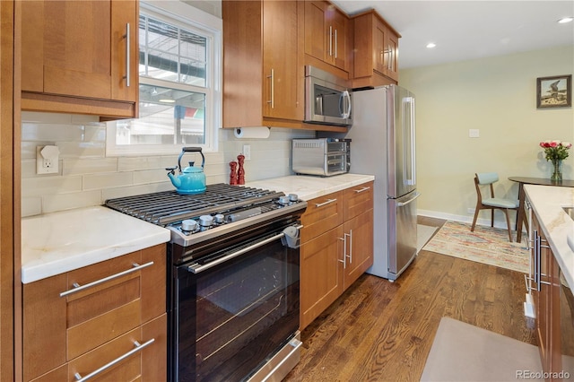 kitchen with decorative backsplash, a toaster, dark wood finished floors, stainless steel appliances, and brown cabinetry