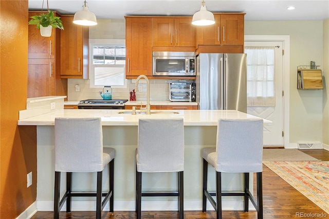 kitchen featuring appliances with stainless steel finishes, light countertops, a kitchen bar, a sink, and backsplash