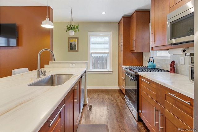 kitchen with stainless steel appliances, a sink, hanging light fixtures, brown cabinets, and tasteful backsplash