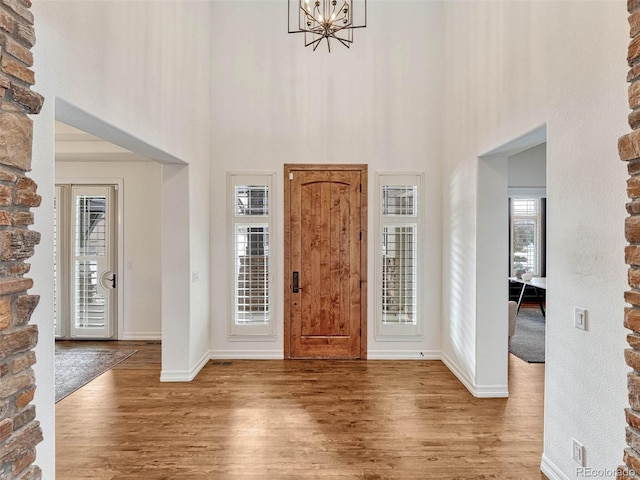 foyer featuring a high ceiling, an inviting chandelier, plenty of natural light, and wood-type flooring