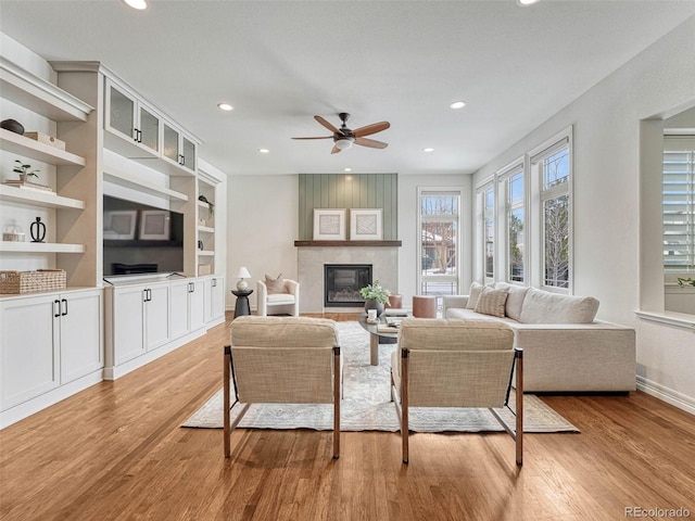 living room with built in features, ceiling fan, a large fireplace, and light hardwood / wood-style floors