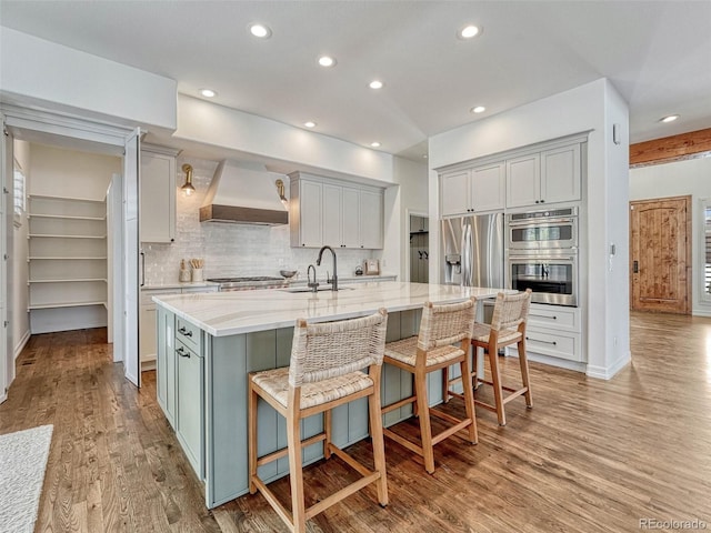 kitchen featuring custom range hood, sink, light stone counters, a kitchen bar, and a center island with sink