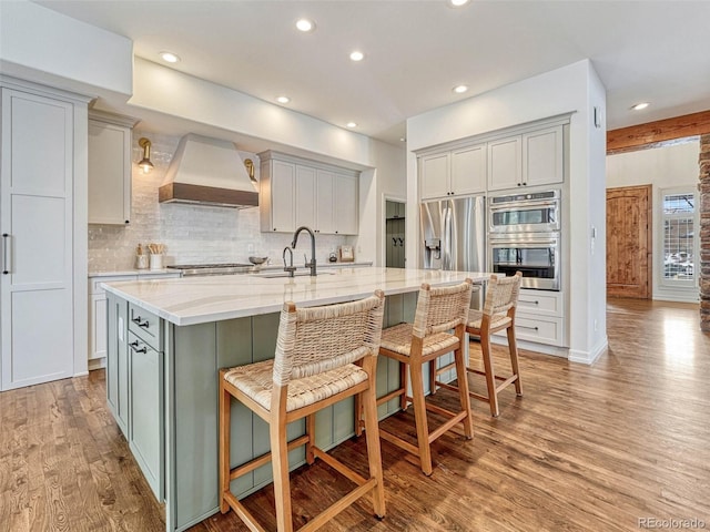 kitchen with a spacious island, appliances with stainless steel finishes, premium range hood, light stone countertops, and a breakfast bar