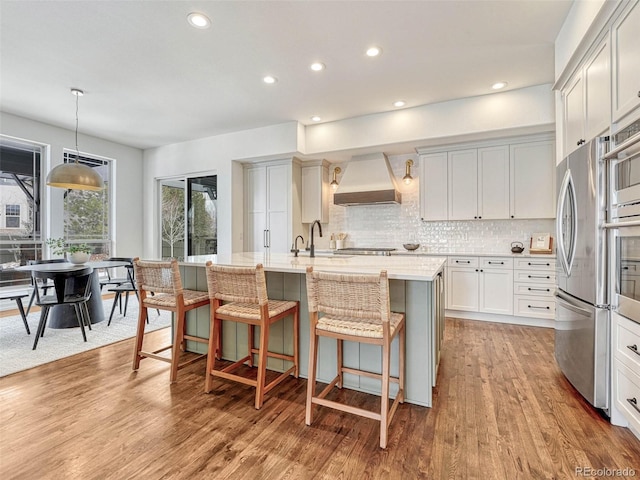 kitchen with decorative light fixtures, an island with sink, a breakfast bar, light hardwood / wood-style flooring, and custom range hood