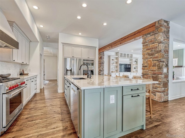 kitchen featuring a large island with sink, white cabinets, stainless steel appliances, decorative backsplash, and premium range hood