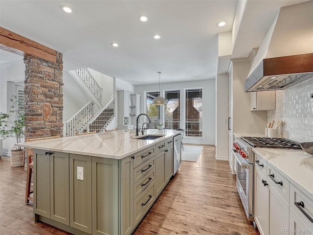 kitchen featuring custom exhaust hood, appliances with stainless steel finishes, sink, pendant lighting, and a center island with sink