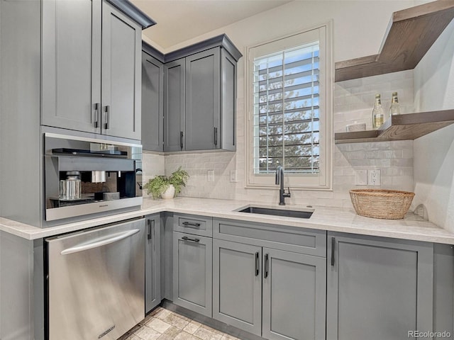 kitchen featuring stainless steel dishwasher, sink, gray cabinetry, light stone counters, and decorative backsplash