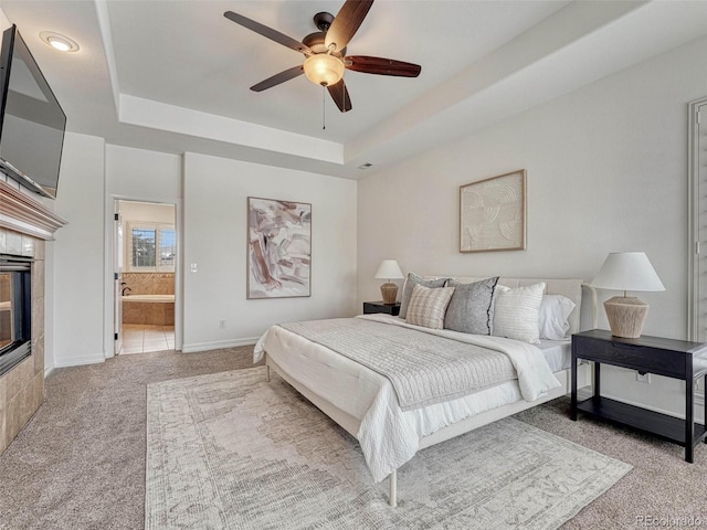 carpeted bedroom with ceiling fan, ensuite bathroom, a raised ceiling, and a fireplace