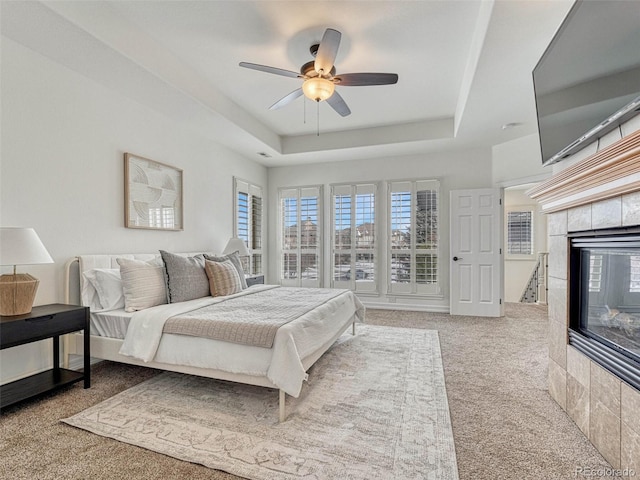 carpeted bedroom featuring a tile fireplace, ceiling fan, and a raised ceiling