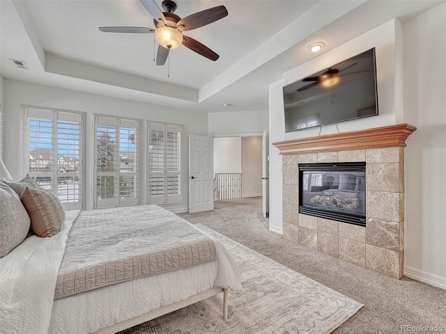 carpeted bedroom featuring ceiling fan, a raised ceiling, and a tiled fireplace