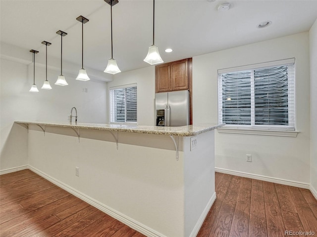 kitchen with stainless steel refrigerator with ice dispenser, decorative light fixtures, a kitchen bar, and kitchen peninsula