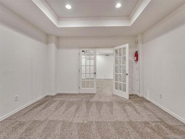 carpeted empty room with ornamental molding, a raised ceiling, and french doors