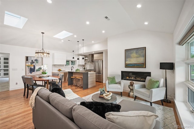 2998 S Adams St, Denver, CO 80210 - living area with a skylight, a glass covered fireplace, vaulted ceiling, light wood-style flooring, and a chandelier