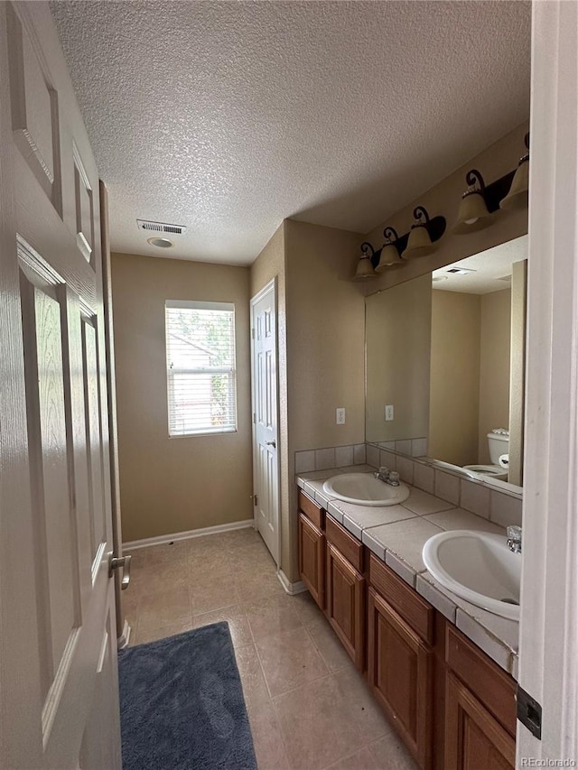 9616 Nucla St, Commerce City, CO 80022 - full bath featuring double vanity, toilet, a textured ceiling, tile patterned flooring, and baseboards