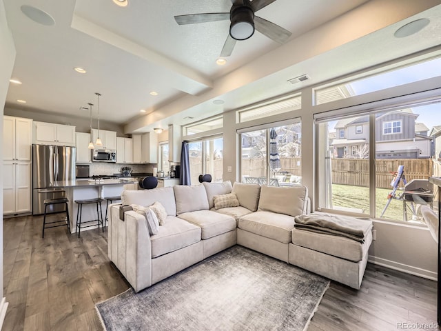 living room with dark wood-style floors, a wealth of natural light, visible vents, and baseboards