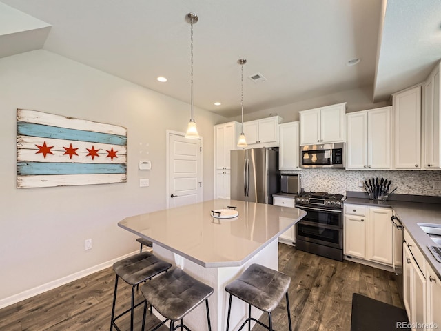 kitchen featuring appliances with stainless steel finishes, dark wood-style flooring, decorative backsplash, and a breakfast bar area