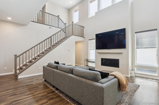 10557 Eby Cir, Lone Tree, CO 80124 - living room featuring stairs, dark wood-type flooring, a towering ceiling, a glass covered fireplace, and recessed lighting