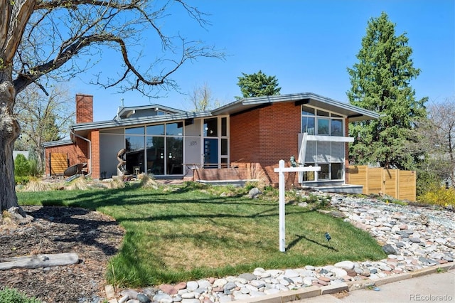 3895 Chimayo Rd, Littleton, CO 80123 - view of front facade featuring a sunroom, a chimney, a front lawn, and brick siding