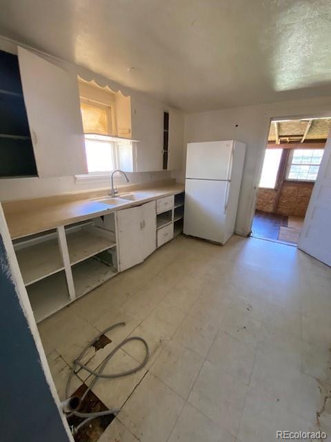 kitchen featuring freestanding refrigerator, open shelves, light countertops, white cabinets, and a sink