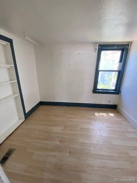 spare room with baseboards, visible vents, built in shelves, and light wood finished floors