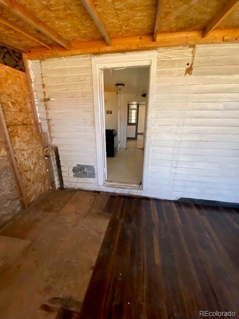 unfurnished room with wood walls, beam ceiling, and dark wood-style floors