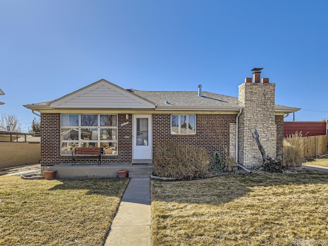 view of front of house with a shingled roof, a chimney, fence, a front lawn, and brick siding