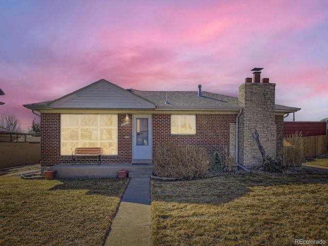 view of front of house with brick siding, roof with shingles, a chimney, and a front yard