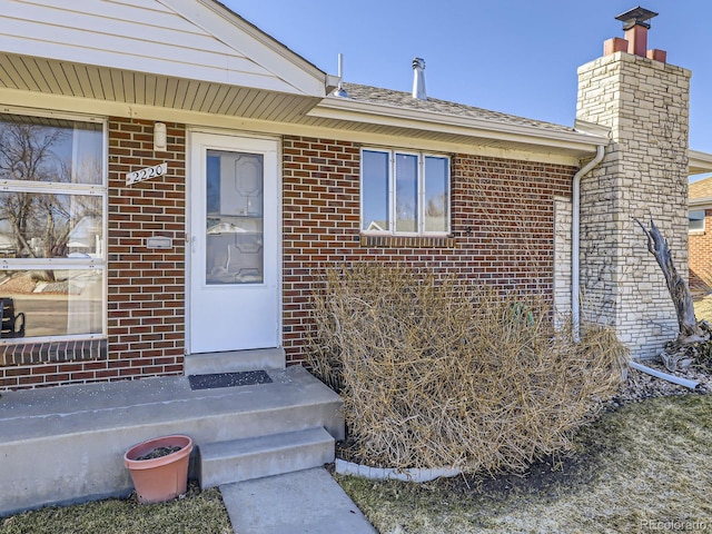 doorway to property featuring a chimney and brick siding