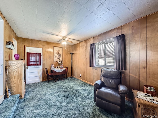 sitting room with carpet, wooden walls, and a ceiling fan