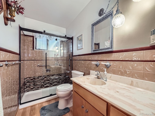 bathroom with wainscoting, toilet, vanity, a shower stall, and tile walls