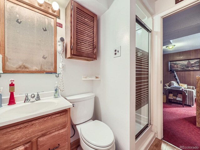 full bathroom with wooden walls, a shower stall, toilet, and vanity