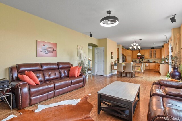 9536 W Avalon Dr, Littleton, CO 80127 - living room featuring a chandelier, arched walkways, light wood-type flooring, and baseboards