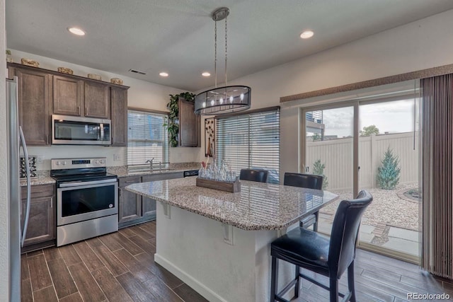 kitchen featuring wood finish floors, a healthy amount of sunlight, appliances with stainless steel finishes, a center island, and a kitchen bar