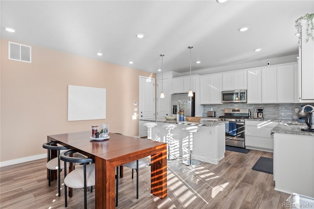 kitchen with light wood-type flooring, a center island, hanging light fixtures, stainless steel appliances, and white cabinets