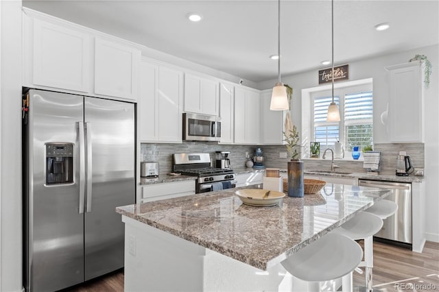 kitchen featuring a kitchen island, hanging light fixtures, stainless steel appliances, sink, and white cabinetry