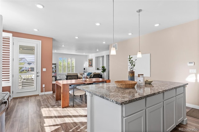 kitchen featuring light wood-type flooring, stone countertops, pendant lighting, gray cabinetry, and a center island