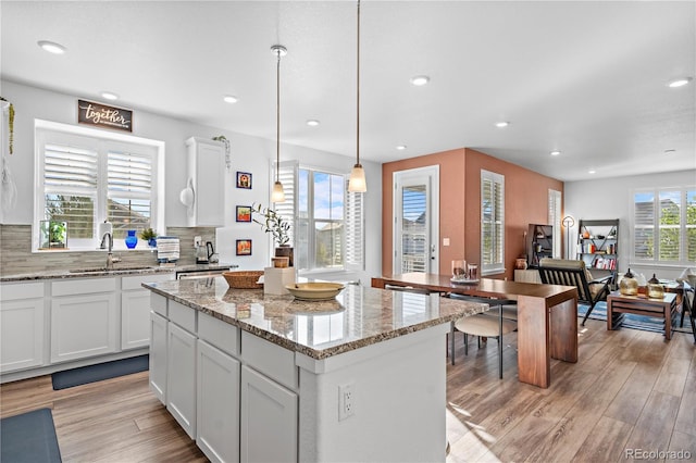 kitchen featuring light stone counters, white cabinetry, a center island, light hardwood / wood-style floors, and decorative light fixtures