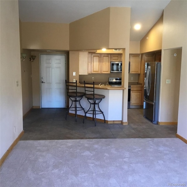 kitchen with tile patterned floors, carpet floors, appliances with stainless steel finishes, a breakfast bar area, and baseboards