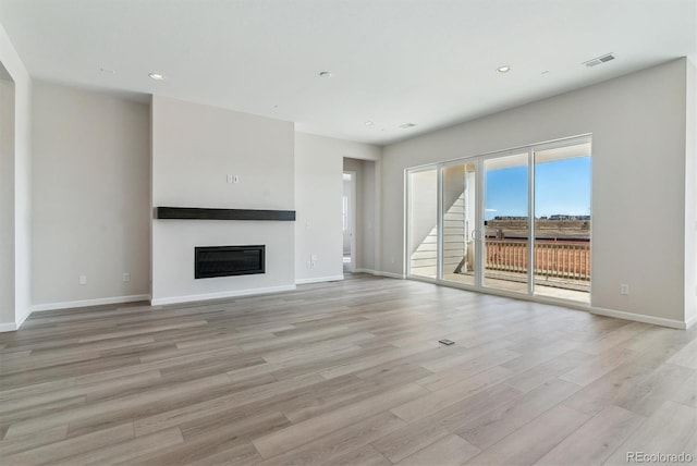 unfurnished living room featuring light wood-style flooring, visible vents, baseboards, and a glass covered fireplace