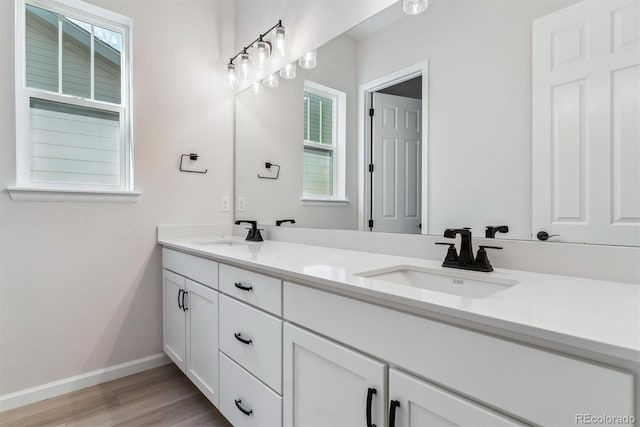 full bath featuring double vanity, wood finished floors, a sink, and baseboards