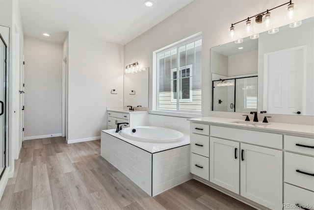 bathroom featuring a garden tub, wood finished floors, two vanities, a sink, and a stall shower