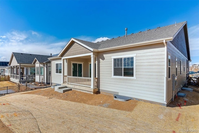 back of property with fence, a porch, and roof with shingles