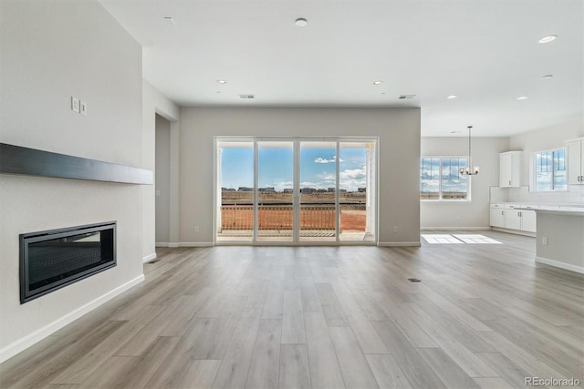 unfurnished living room featuring light wood-type flooring, baseboards, a chandelier, and a glass covered fireplace