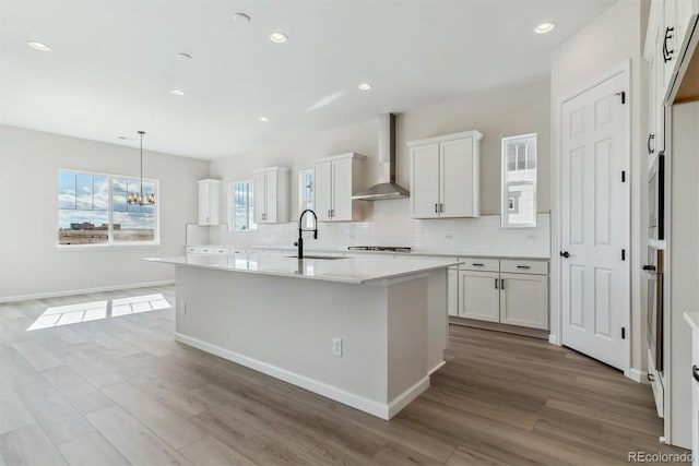 kitchen with wall chimney range hood, tasteful backsplash, a sink, and wood finished floors