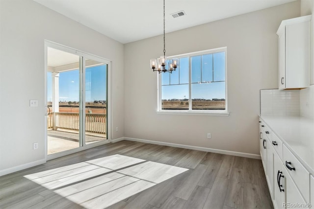 unfurnished dining area featuring light wood-style floors, baseboards, visible vents, and an inviting chandelier