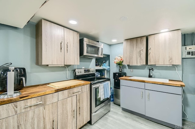 kitchen with light brown cabinets, butcher block counters, sink, light wood-type flooring, and appliances with stainless steel finishes