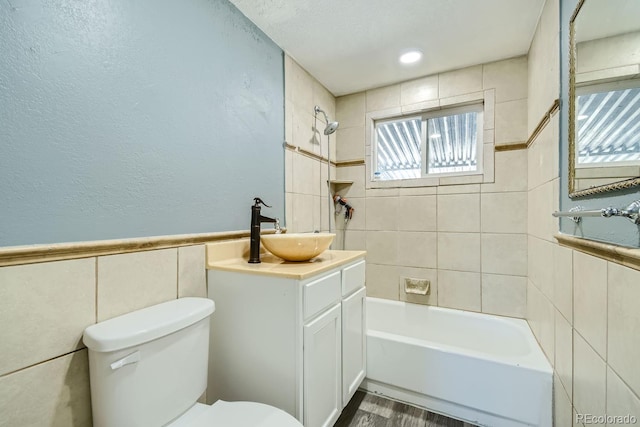 full bathroom with tiled shower / bath, wood-type flooring, tile walls, toilet, and vanity