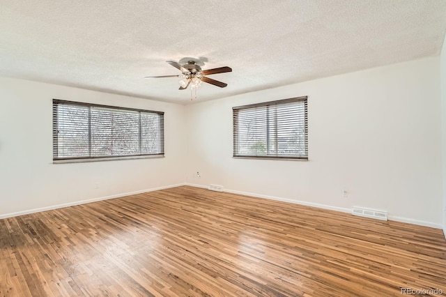 unfurnished room with light wood-type flooring, a ceiling fan, a wealth of natural light, and visible vents