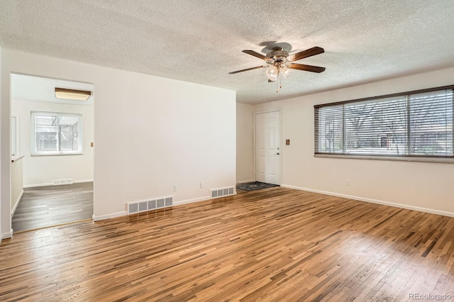 spare room with a wealth of natural light, visible vents, a ceiling fan, and hardwood / wood-style flooring