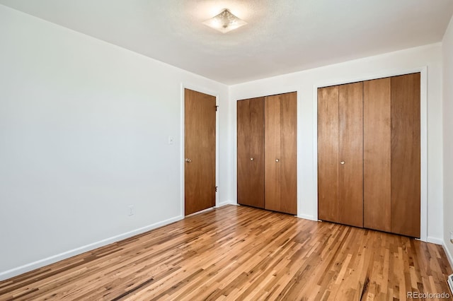 unfurnished bedroom with baseboards, two closets, and light wood-style floors